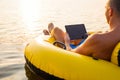 Relaxed man using tablet computer on inflatable ring in the water at sunset Royalty Free Stock Photo