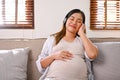 Relaxed and happy Asian pregnant woman listening to music through her headphones Royalty Free Stock Photo