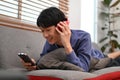 Relaxed Asian man lying on sofa, listening to music through his headphones and using his smartphone Royalty Free Stock Photo