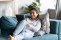 Relaxed indian girl lying on couch holding tablet enjoy e-shopping