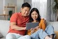 Relaxed japanese family sitting on couch at home, using pad