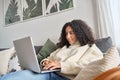 Relaxed latin young woman sitting on sofa using laptop at home surfing.