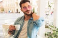 Relaxed man drinking coffee and touching neck looks to side