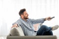 Relaxed man switching channels with remote controller while watching tv at home, relaxing on couch, side view Royalty Free Stock Photo