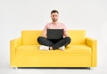 Relaxed man using laptop sitting on yellow sofa over white background Royalty Free Stock Photo