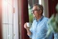 Relaxed mature man at home standing by the window