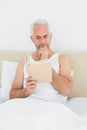 Relaxed mature man reading book in bed Royalty Free Stock Photo