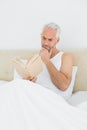 Relaxed mature man reading book in bed Royalty Free Stock Photo