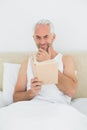 Relaxed mature man reading book in bed Royalty Free Stock Photo
