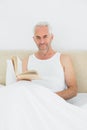 Relaxed mature man reading book in bed Royalty Free Stock Photo