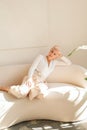 Relaxed mature woman sitting on sofa at home, smiling happily. Portrait of comfortable lady with blonde, short hair Royalty Free Stock Photo