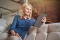 Relaxed mature woman smiling while reading e book using digital tablet pc, relaxing on a couch at home in modern Royalty Free Stock Photo