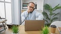 Relaxed middle age businessman engaging in a serious phone conversation while working on his laptop at the office Royalty Free Stock Photo