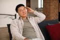 Relaxed middle aged asian man in wireless headphones with closed eyes sitting on sofa, enjoying music, free space Royalty Free Stock Photo