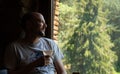 Relaxed middle-aged man with a glass of white wine in his hand illuminated by a dim evening light looking out a window Royalty Free Stock Photo