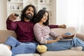 Relaxed millennial couple chilling at home, watching tv, using laptop Royalty Free Stock Photo