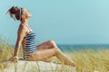 Relaxed modern woman in striped swimsuit sitting on seacoast Royalty Free Stock Photo