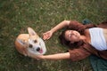 Relaxed moment captured as a woman lies on the grass with to a Corgi dog