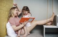 Relaxed mother and little daughter sitting together on cozy stairs in living room with book in their hands Royalty Free Stock Photo