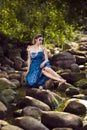 Relaxed Positive Lady Posing As Sea Mermaid in Artistic Blue Dress And Strasses on Face Sitting in Wet Dress on Rocky Shore