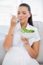 Relaxed pretty woman eating healthy salad sitting on sofa Royalty Free Stock Photo