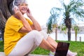 Relaxed senior woman with headphones sitting outdoors  smiling. Laptop computer on bench Royalty Free Stock Photo