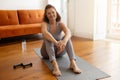 Relaxed senior woman taking break after domestic training, sitting on yoga mat Royalty Free Stock Photo