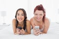 Relaxed smiling female friends text messaging on bed Royalty Free Stock Photo