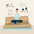A relaxed smiling man sits in his room or apartment on a soft sofa with his legs crossed and meditates.