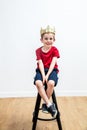 Relaxed smiling young boy with a crown seated on stool