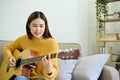 Relaxed Asian female singing and playing guitar in her home living room alone Royalty Free Stock Photo