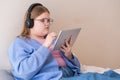 Relaxed teen girl in headphones completing online tasks on school website via tablet