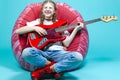 Relaxed Teenager Guitar Player With Red Bass Guitar Posing In Casual White Shirt With Smiling Facial Expression While Sitting on