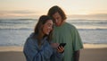 Relaxed teenagers looking phone at evening ocean. Sweethearts listening music Royalty Free Stock Photo