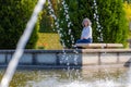 Relaxed and thoughtful mature Mexican woman sitting on a concrete bench, seen through the jets of a functioning fountain