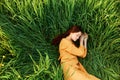 a relaxed woman enjoys summer lying in the tall green grass with her eyes closed. Photo taken from above