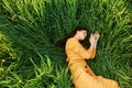 a relaxed woman enjoys summer lying in the tall green grass with her eyes closed. Photo taken from above