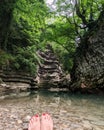 Relaxed woman feet with red pedicure in the background of rocks and caves and azure clear water and green trees Royalty Free Stock Photo