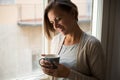 Relaxed woman holding a cup of coffee portrait next to a window