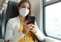 Relaxed woman with KN95 FFP2 face mask using smart phone app. Train passenger with protective mask traveling sitting in business