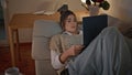 Relaxed woman lounging couch looking laptop at evening home environment zoom on