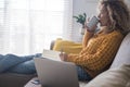 Relaxed and worried adult woman at home with paper and pen and computer laptop sit down on the sofa thinking and. drinking Royalty Free Stock Photo