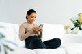 Relaxed young African American woman using crucial mobile phone on sofa couch Royalty Free Stock Photo