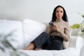 Relaxed young African American woman using crucial mobile phone on sofa couch Royalty Free Stock Photo