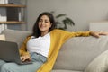 Relaxed young arab lady working from home, sitting on couch and using laptop, enjoying her weekend, surfing on internet Royalty Free Stock Photo