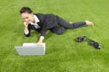 A relaxed young Asian businesswoman lying on grass using her laptop. Conceptual image Royalty Free Stock Photo