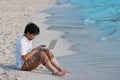Relaxed young Asian man with laptop sitting on sandy of the beach. Internet of things concept Royalty Free Stock Photo