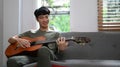 Relaxed young asian man playing acoustic guitar, spending leisure time in bright living room Royalty Free Stock Photo