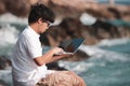 Relaxed young Asian man using laptop at sea shore. Internet of things concept. Royalty Free Stock Photo