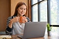 Relaxed young Asian woman sipping a coffee while reading an online content on laptop Royalty Free Stock Photo